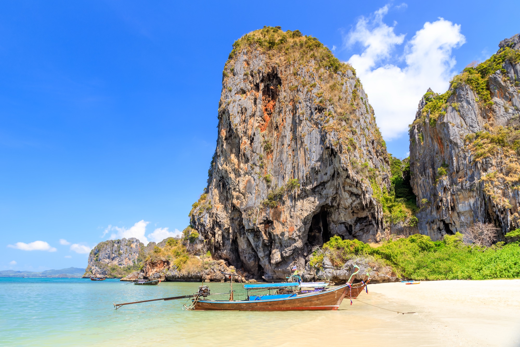 Longtail boat in turquoise water beneath limestone cliffs, Phra Nang Beach, Krabi