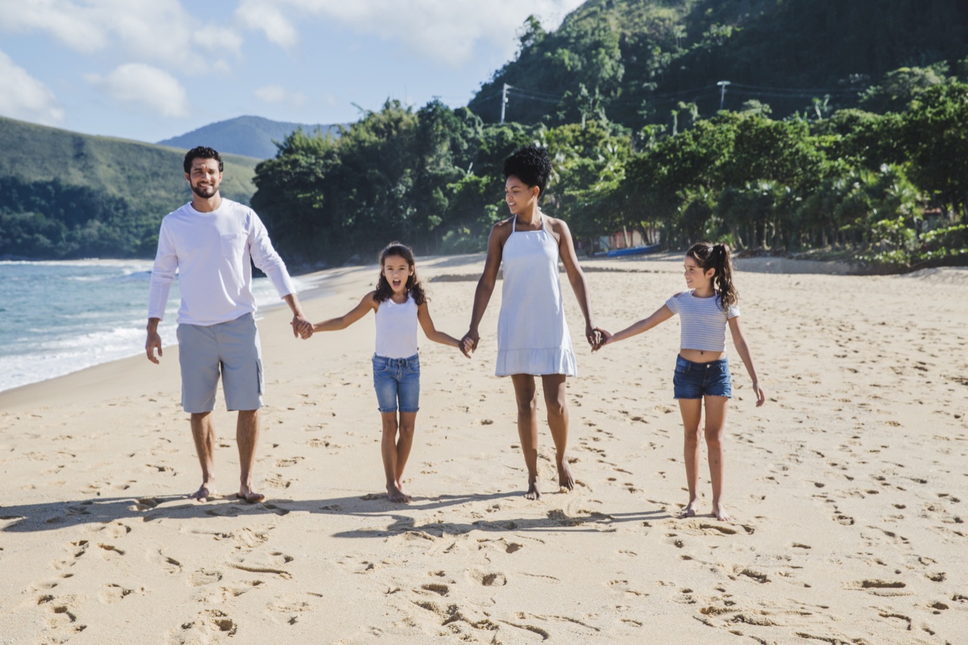 A family with two young daughters walking hand in hand along a sunny beach
